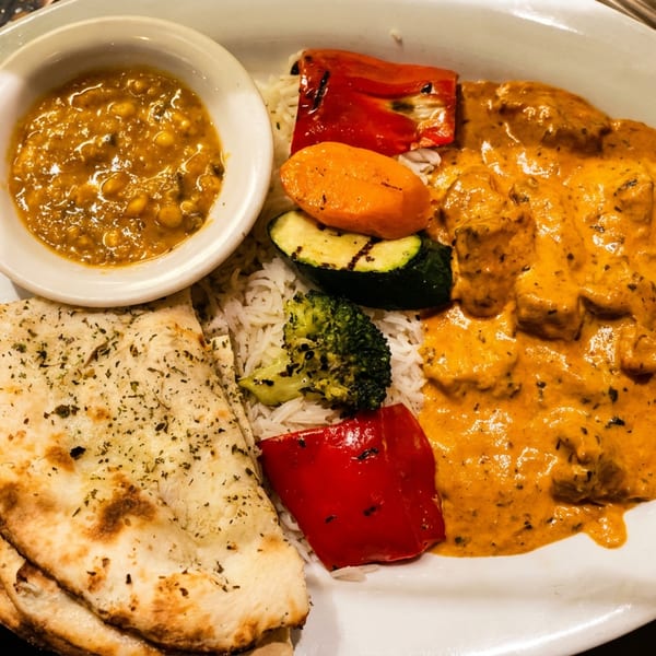 Indian platter with butter chicken, rice, naan, grilled vegetables, and a side of chickpea curry.