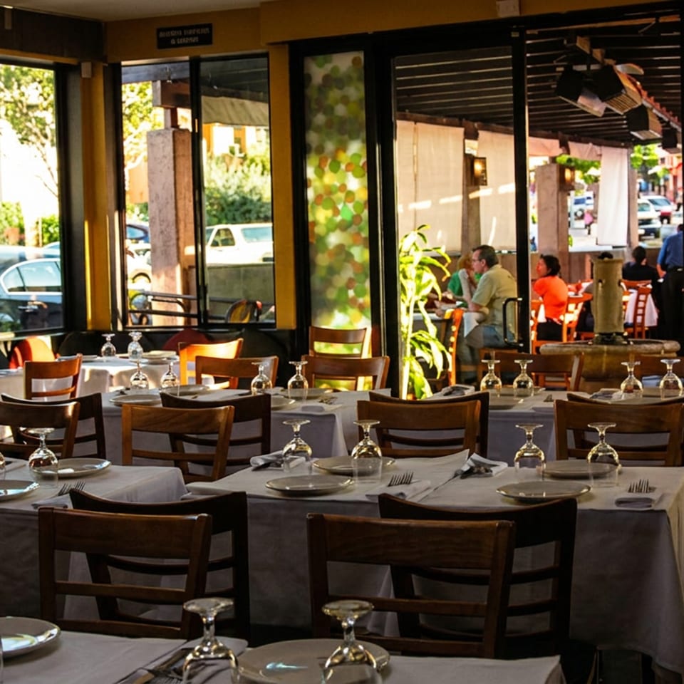 Sunny restaurant dining room with set tables, wooden chairs, and an outdoor patio with diners visible.