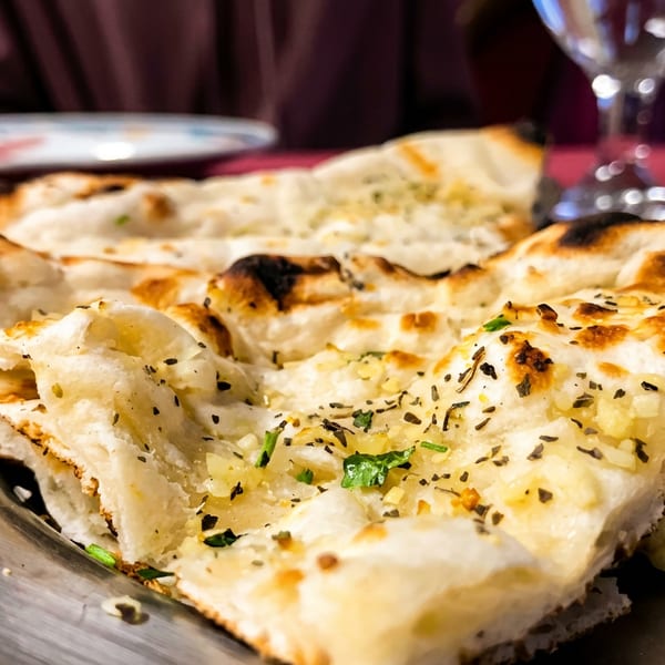 Freshly baked, golden-brown garlic naan bread with herbs on a metal plate.
