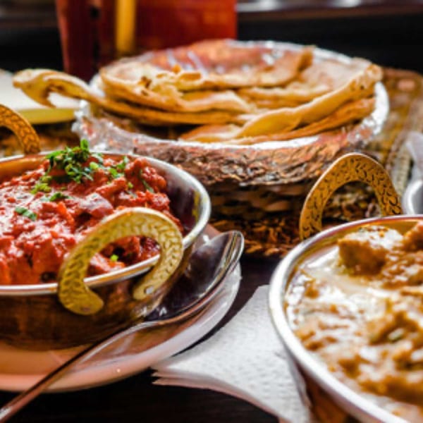 Two vibrant Indian curries, flatbread, and rice served in traditional metal bowls.