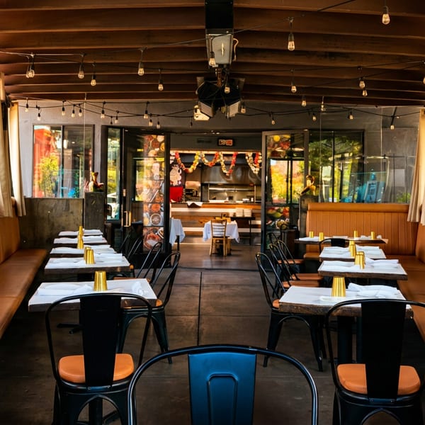 Cozy restaurant dining room with long orange booths, set tables, string lights, and an open kitchen.